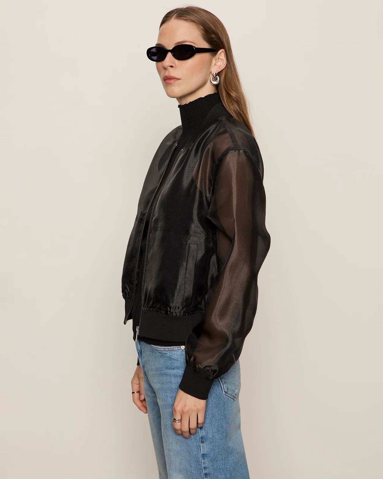 woman wearing a black sheer organza jacket over a black turtleneck and blue jeans