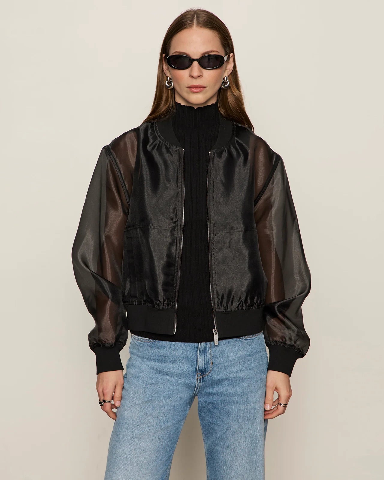 woman wearing a black sheer organza jacket over a black turtleneck and blue jeans