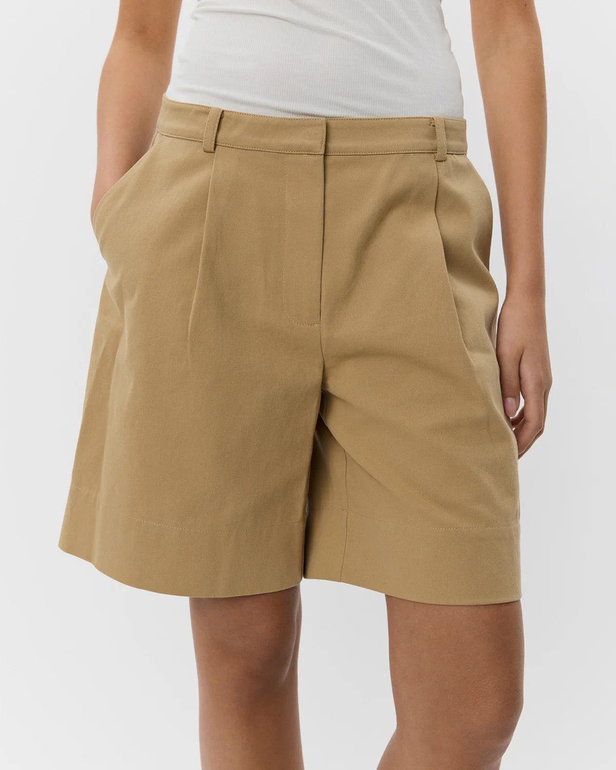 A pair of beige knee-length shorts with a wide cuffed edge, side pockets, and one back pocket, made of cotton.
