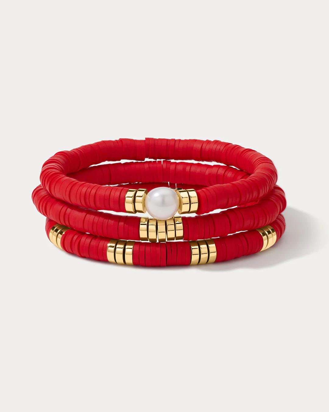 a set of red beaded bracelets with gold beads and a pearl charm