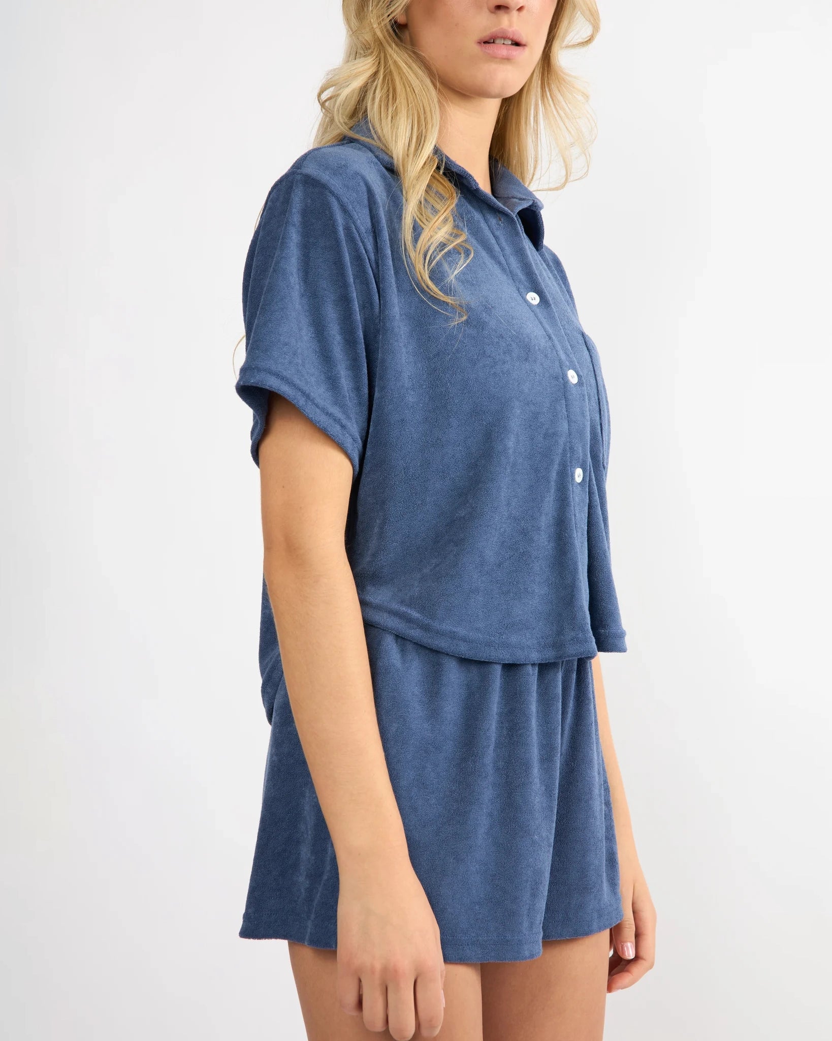 woman wearing button down terry cloth top and matching short set in blue