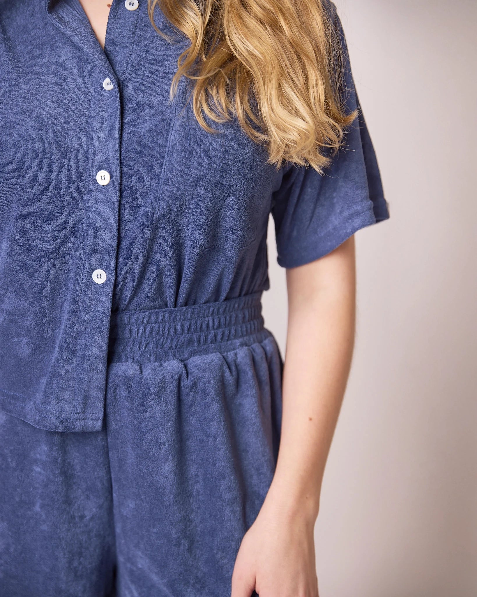woman wearing button down terry cloth top and matching short set in blue