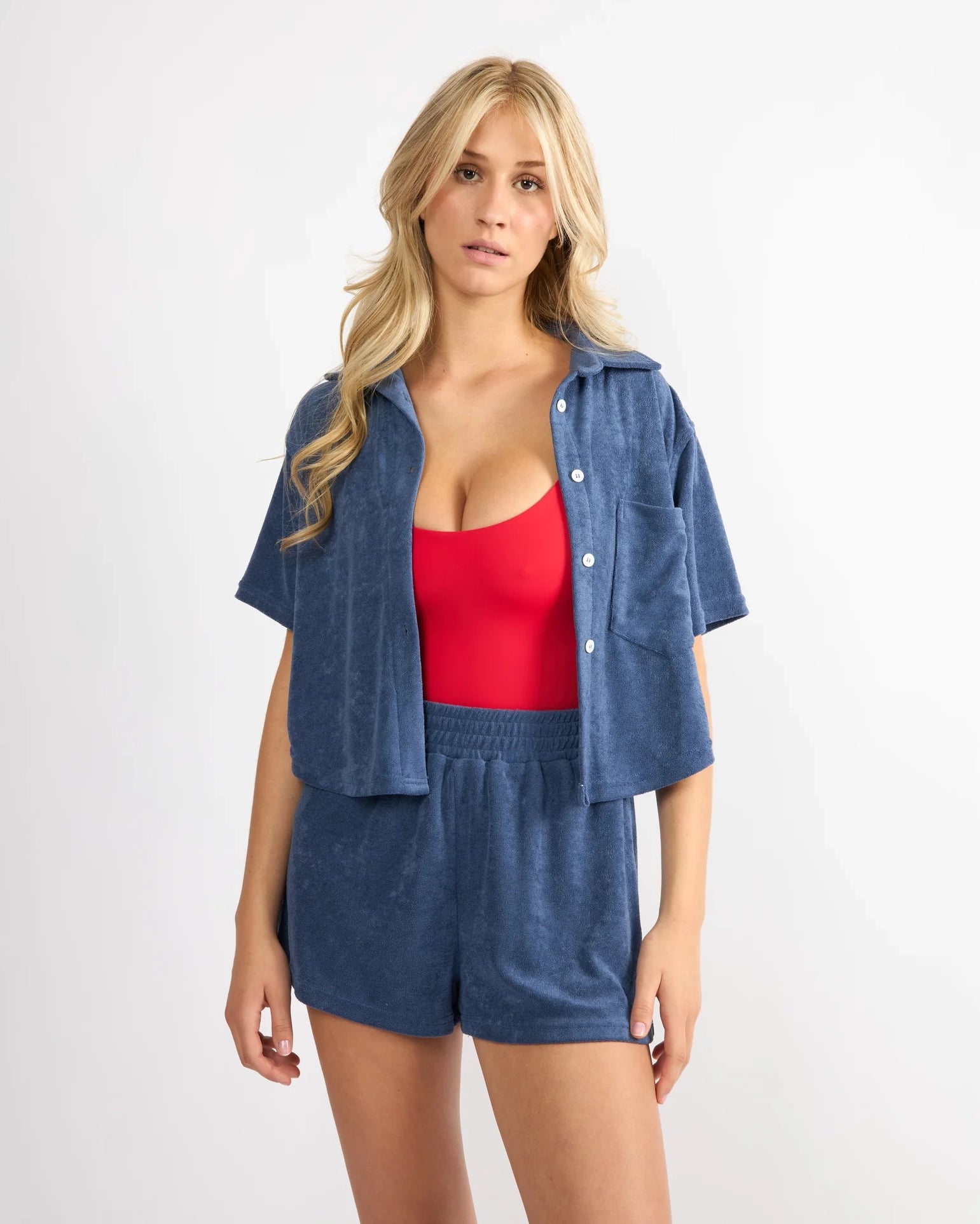 woman wearing open button down terry cloth top over swimsuit with matching shorts as a set in blue