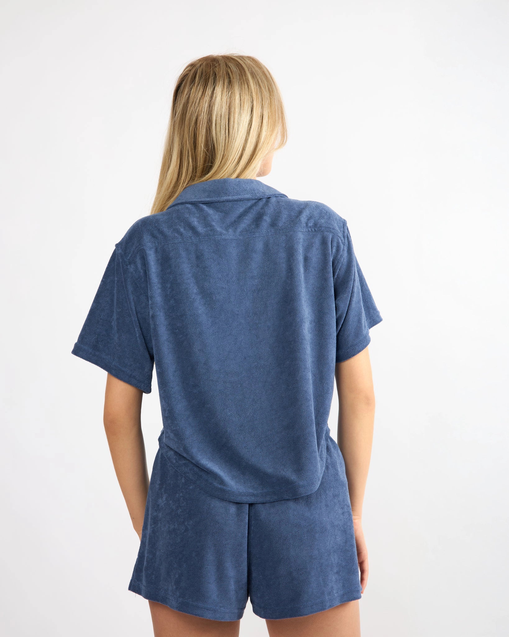 woman wearing button down terry cloth top and matching short set in blue