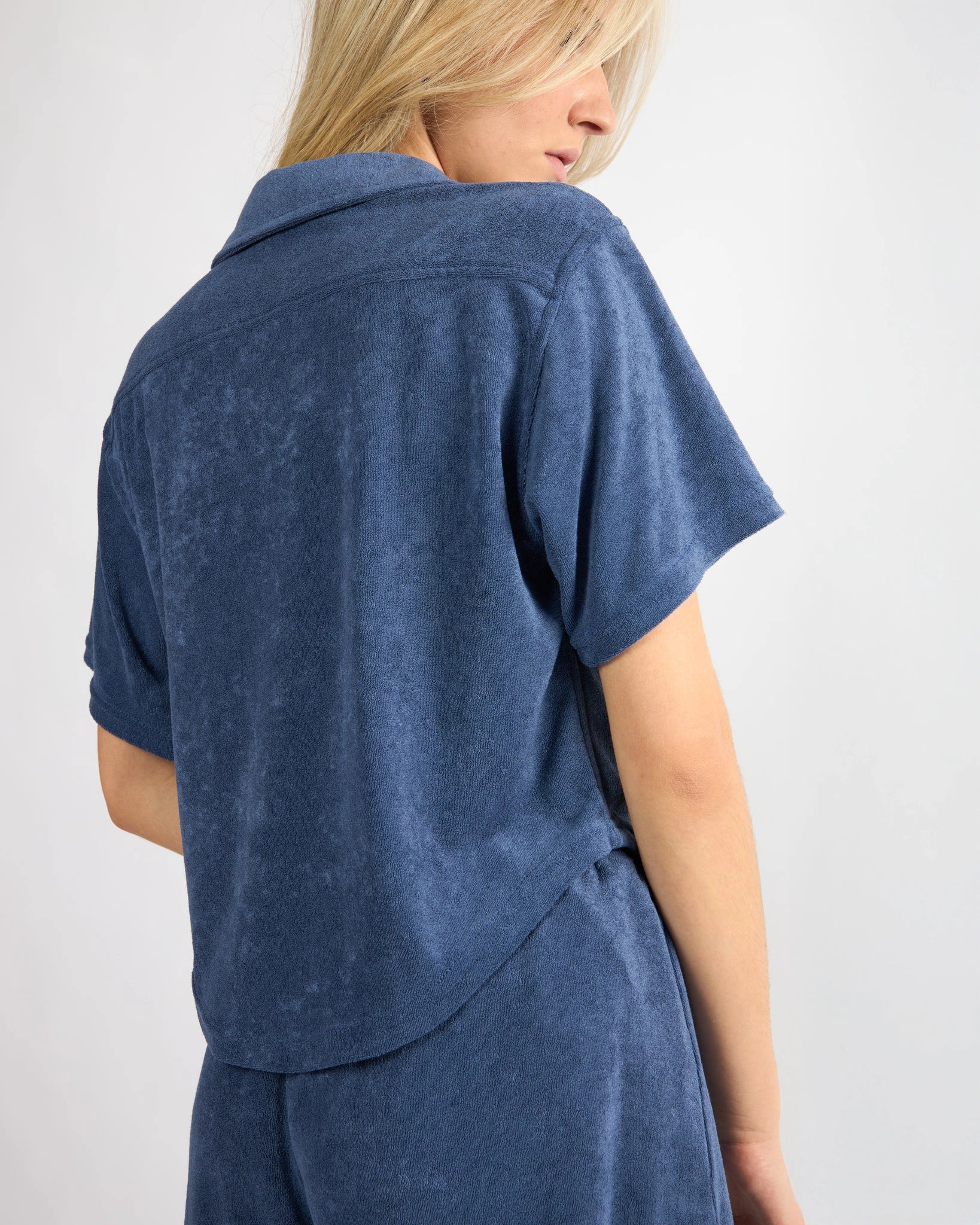 woman wearing button down terry cloth top and matching short set in blue