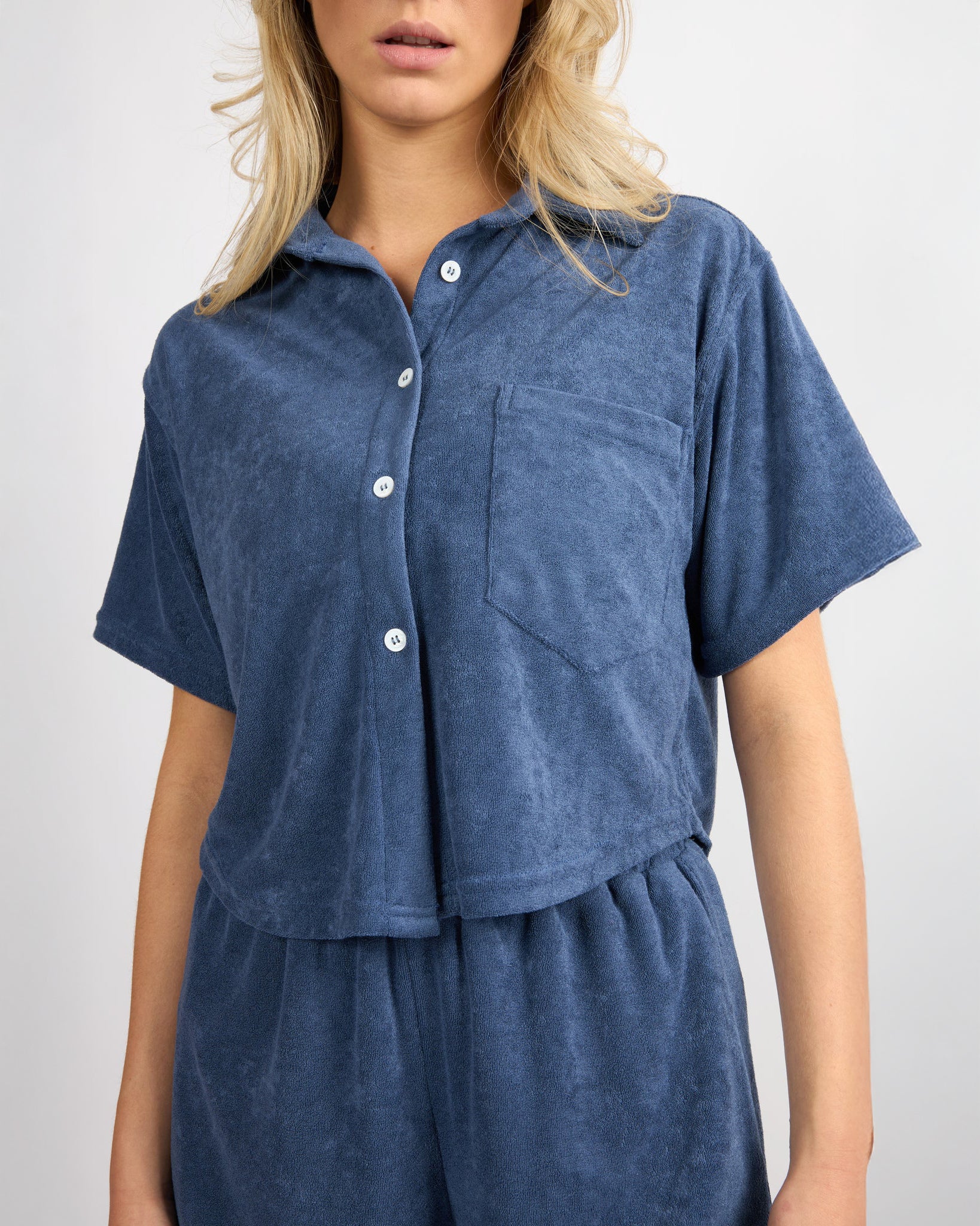 woman wearing button down terry cloth top and matching short set in blue