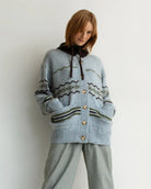 woman wearing a geometric fairisle patterned button down cardigan sweater in light. blue with green accents