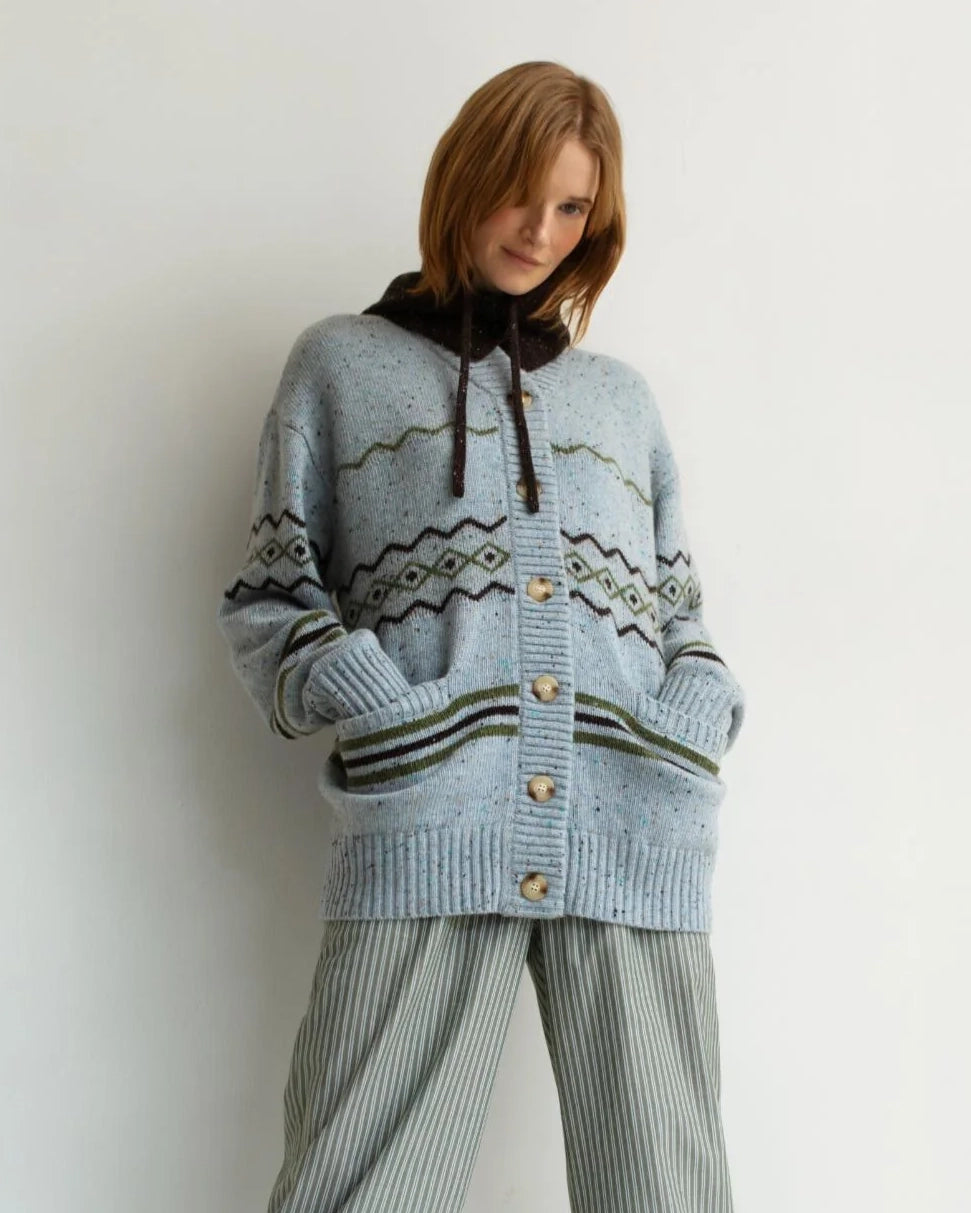 woman wearing a geometric fairisle patterned button down cardigan sweater in light. blue with green accents