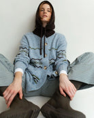 woman wearing a geometric fairisle patterned button down cardigan sweater in light. blue with green accents