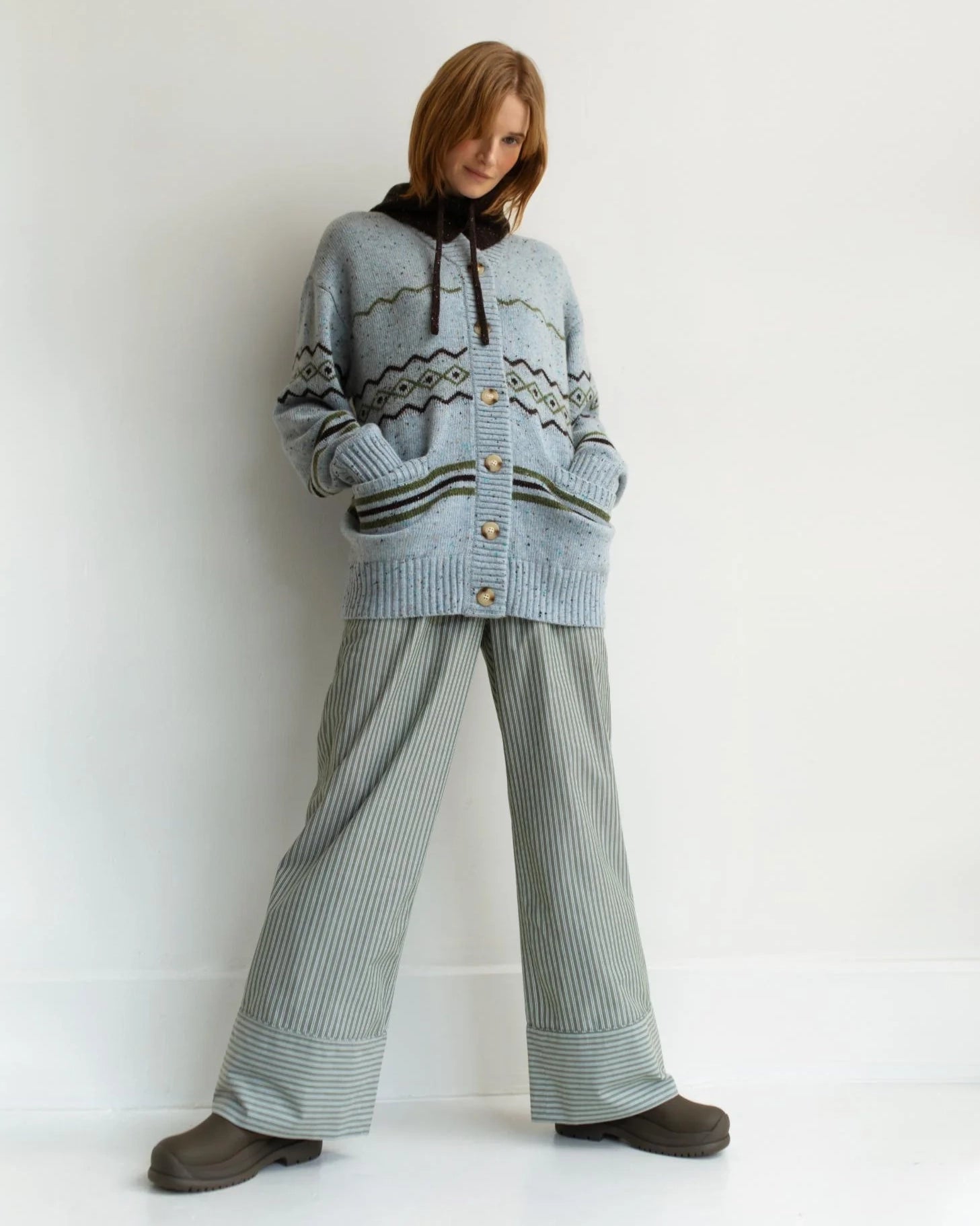 woman wearing a geometric fairisle patterned button down cardigan sweater in light. blue with green accents