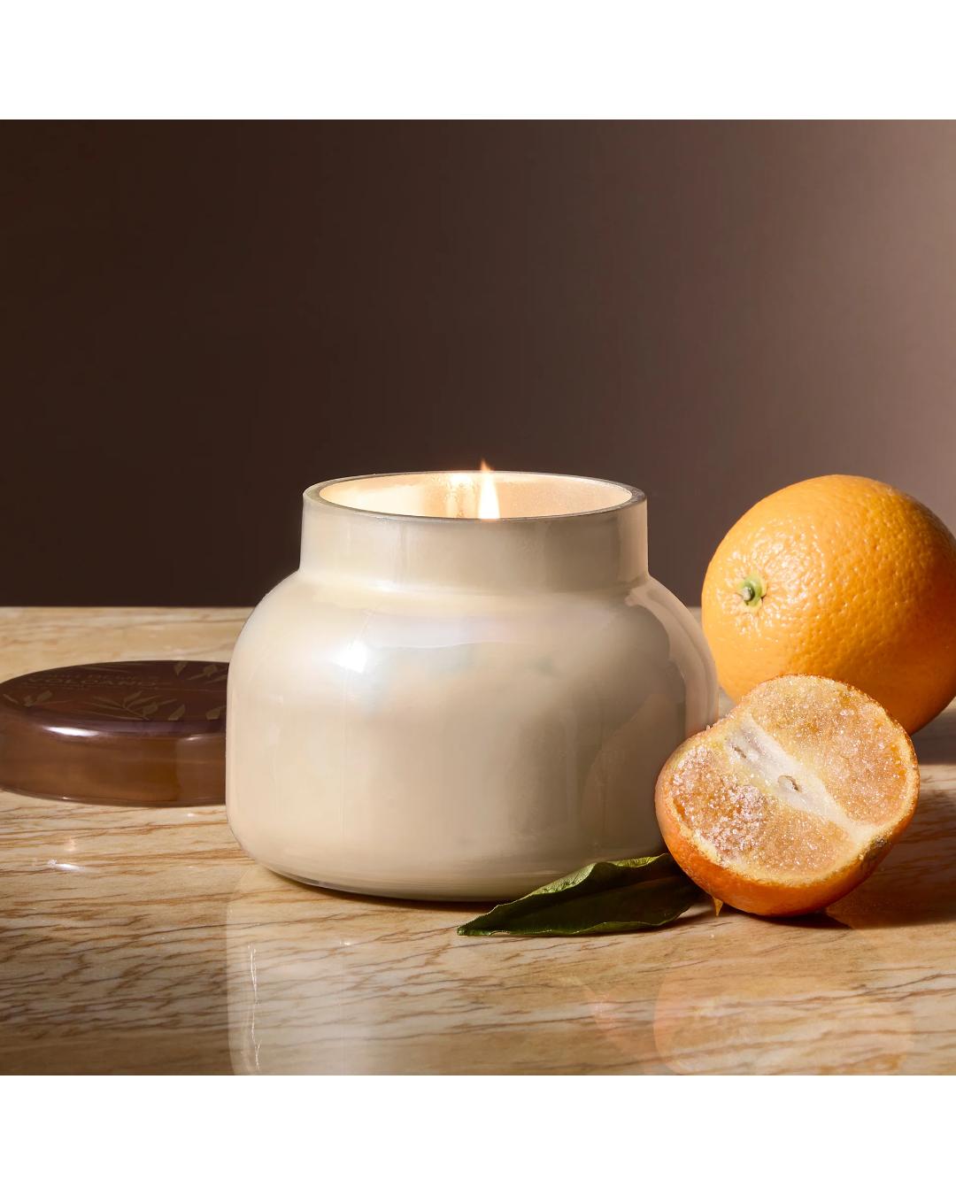 Ceramic diffuser with a lit candle on a wooden surface with oranges and leaves.