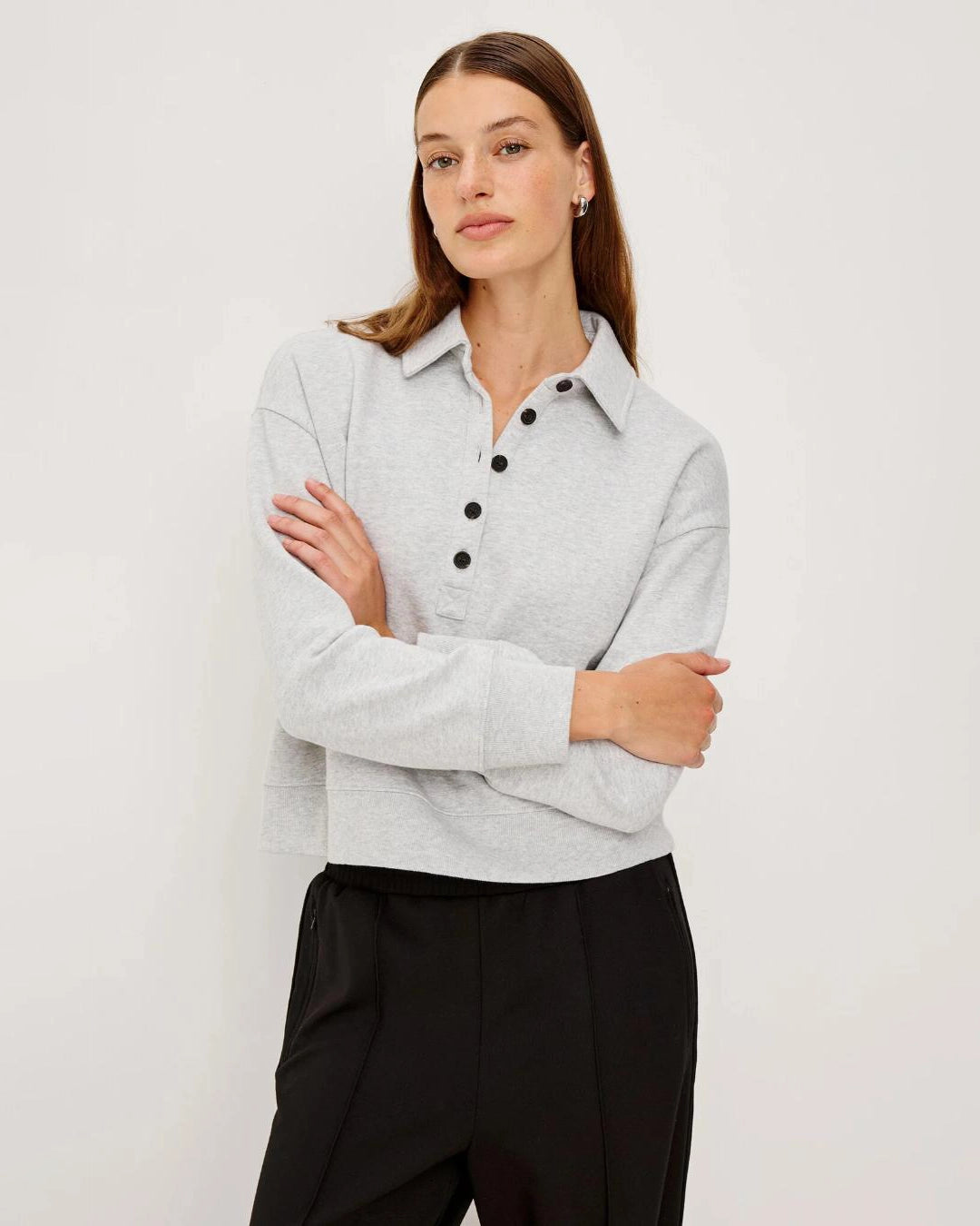 Woman wearing a light gray knit long-sleeve sweater with black buttons halfway down