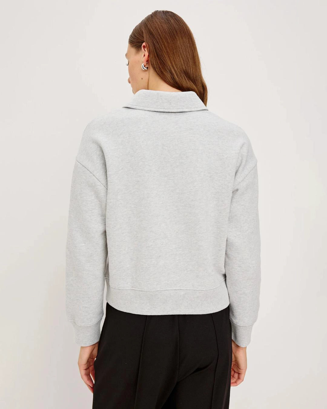 Woman wearing a light gray knit long-sleeve sweater with black buttons halfway down