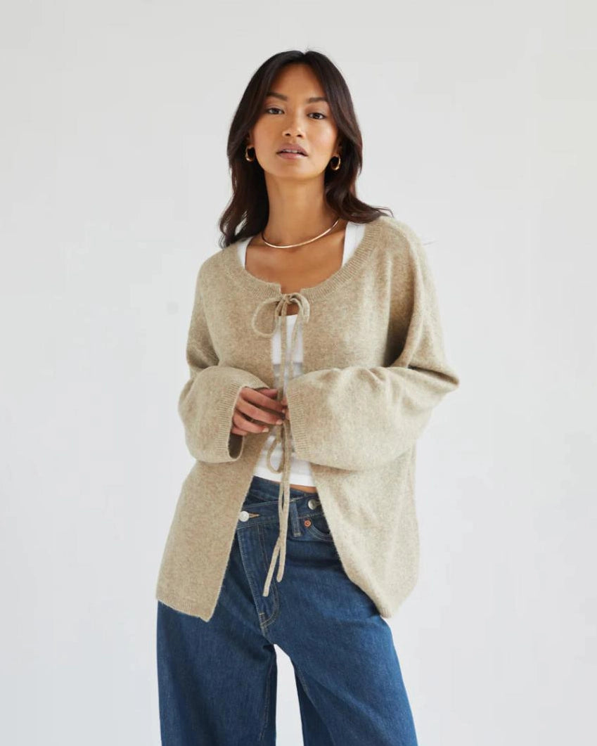 a woman wears a reversible cardigan sweater in beige with bow closures