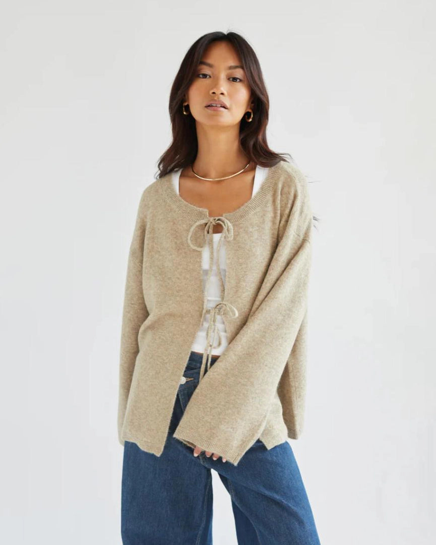 a woman wears a reversible cardigan sweater in beige with bow closures