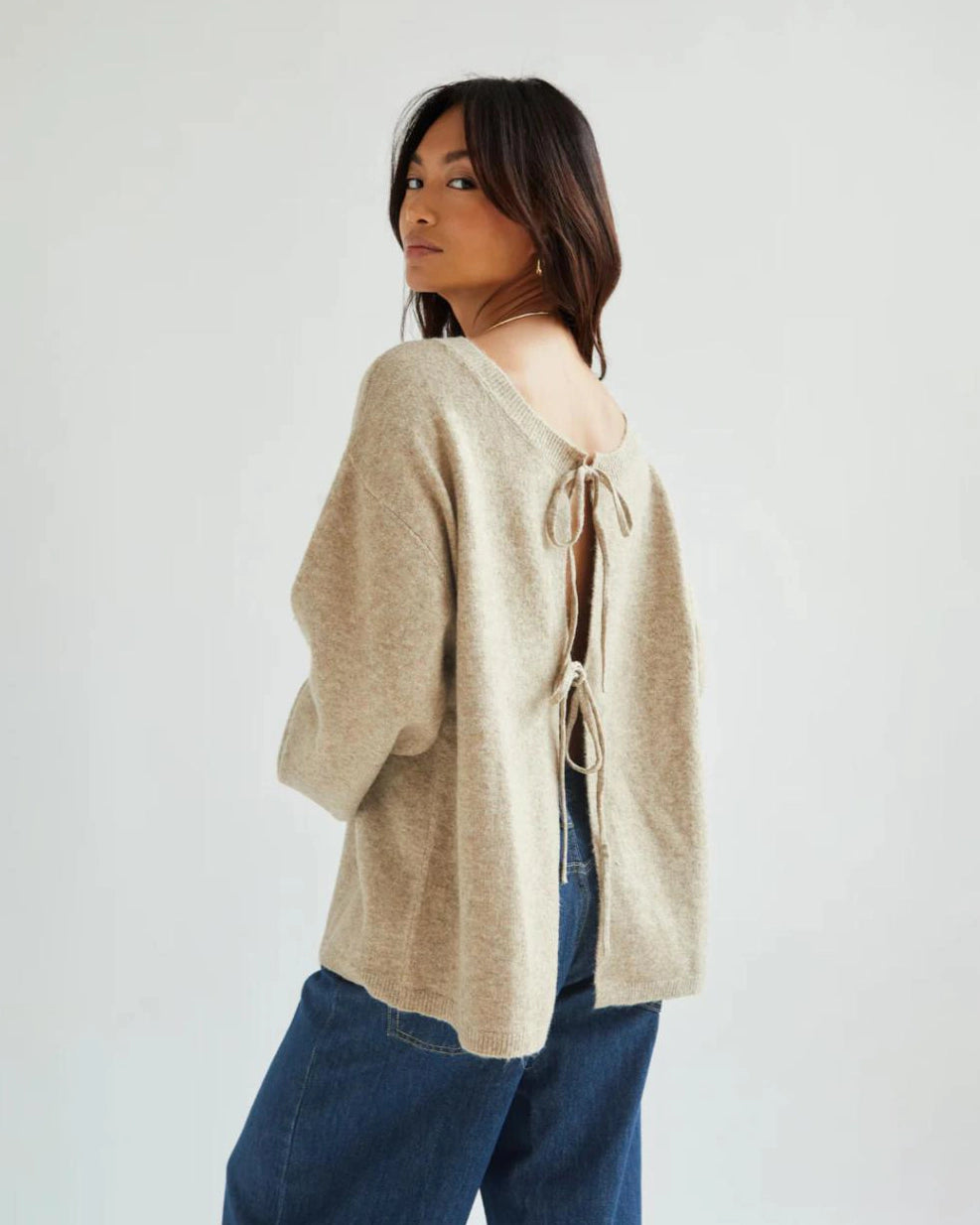 a woman wears a reversible cardigan sweater in beige with bow closures