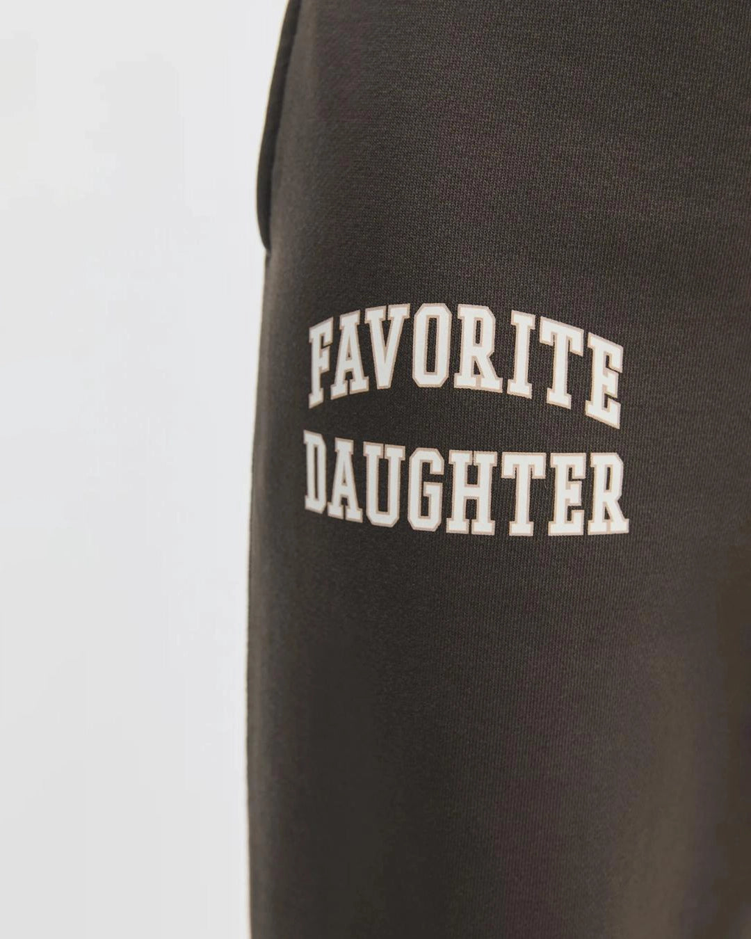 close up of brown sweatpants with 'favourite daughter' in varsity letters on them