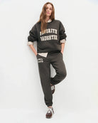 woman wearing dark brown sweatpants with 'favourite daughter' in varsity letters on them