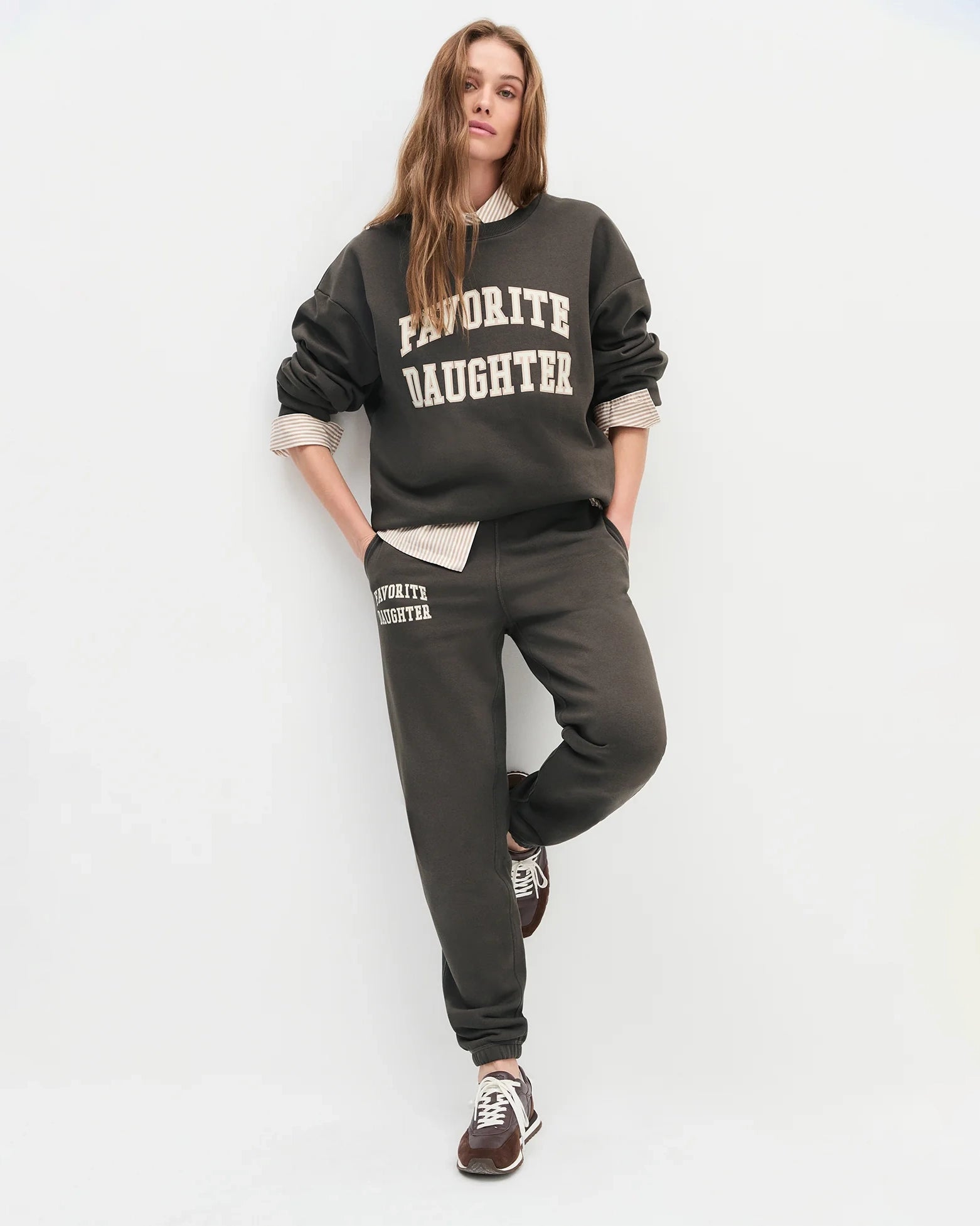 woman wearing dark brown sweatpants with 'favourite daughter' in varsity letters on them