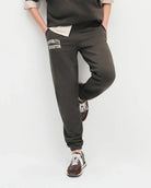 woman wearing dark brown sweatpants with 'favourite daughter' in varsity letters on them