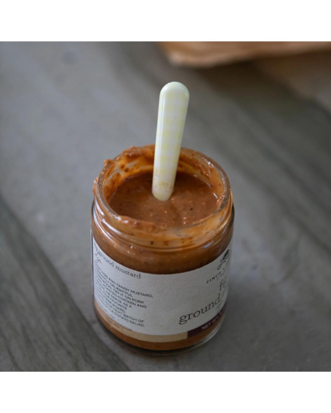 Jar of mustard with a used spoon on a wooden surface