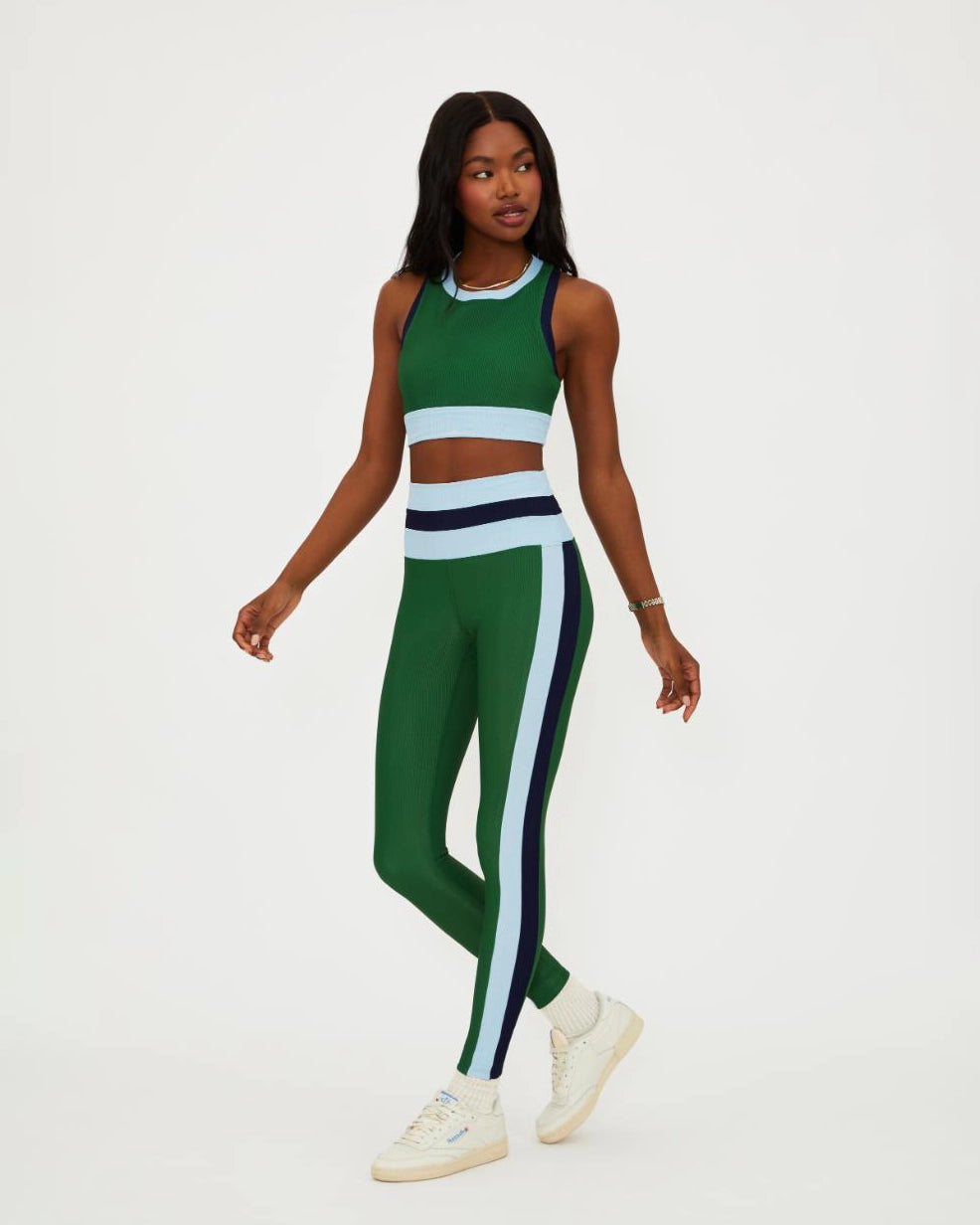 A woman wears a green racerback crop tank with light blue and navy on the bottom and sides