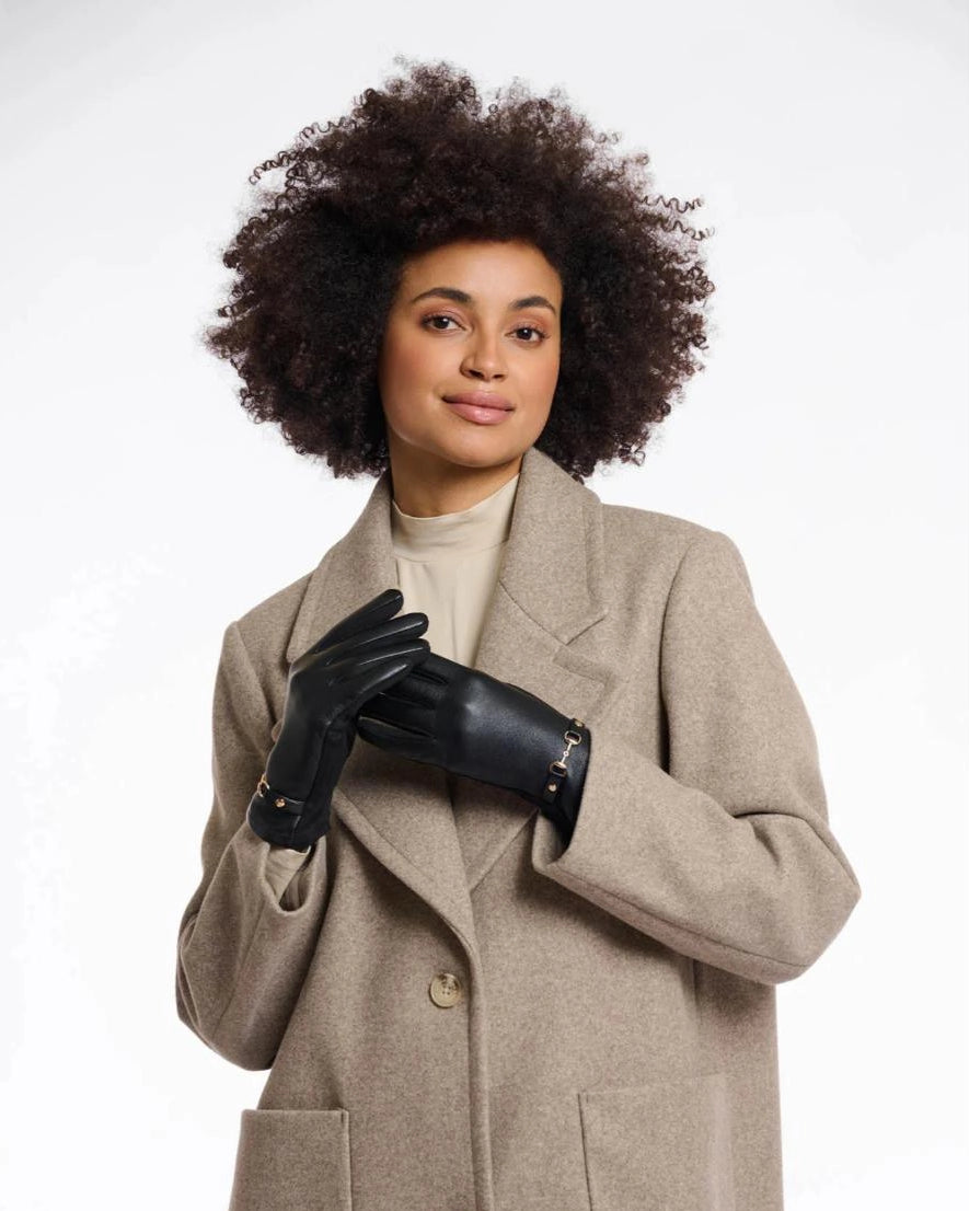 a woman wears a pair of faux leather gloves in black with a gold horsebit detail on the wrist