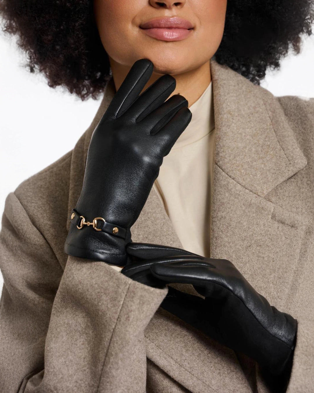 a woman wears a pair of faux leather gloves in black with a gold horsebit detail on the wrist