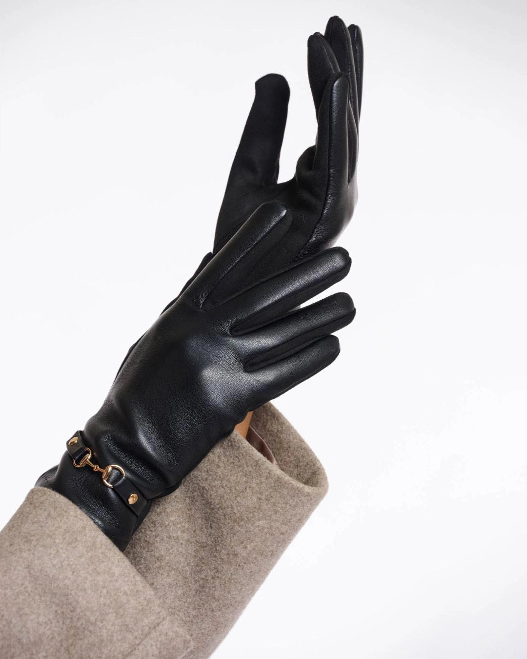 a woman wears a pair of faux leather gloves in black with a gold horsebit detail on the wrist
