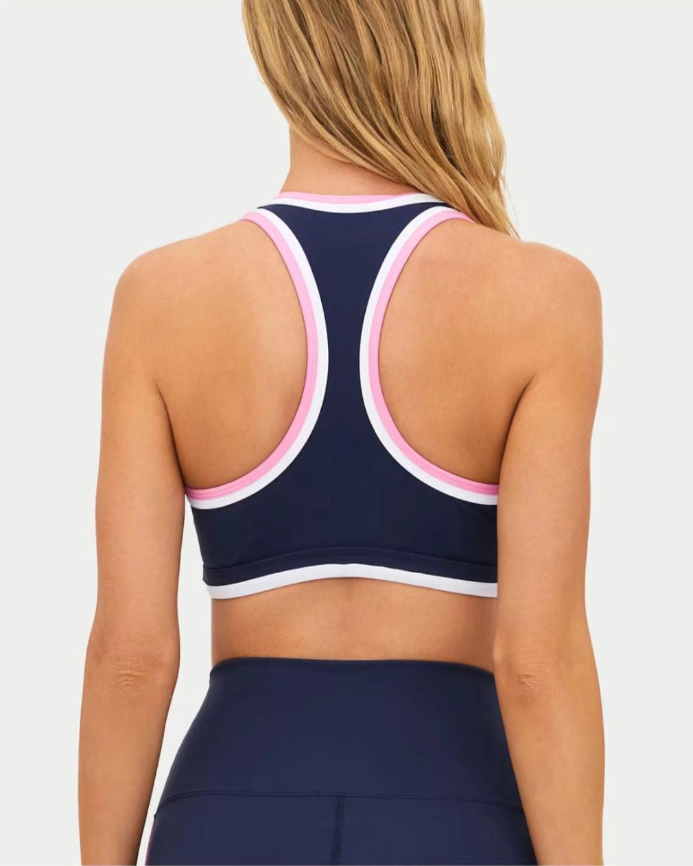 a woman wears a navy racerback sports bra with pink and white outline