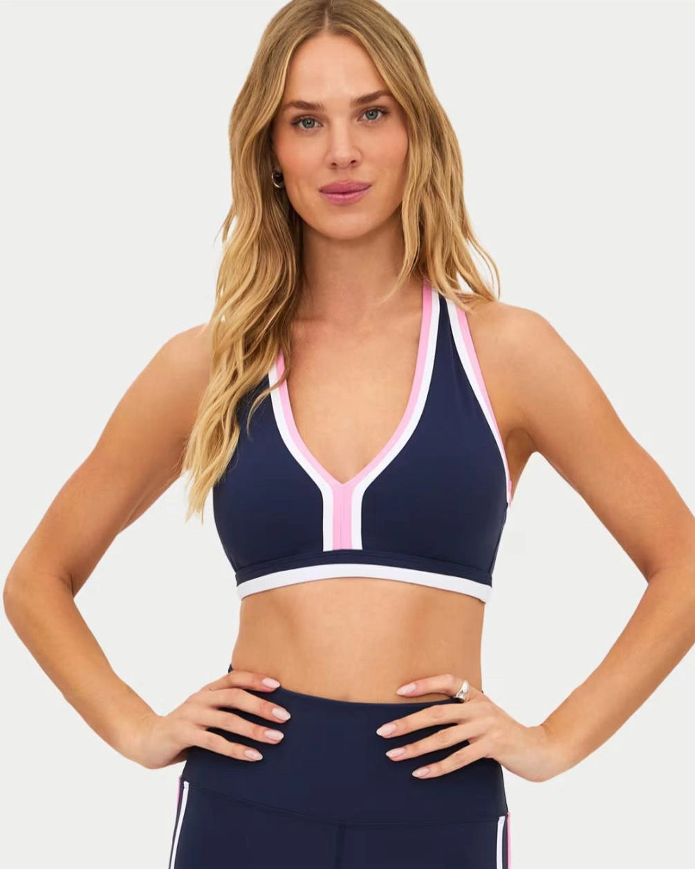 a woman wears a navy racerback sports bra with pink and white outline