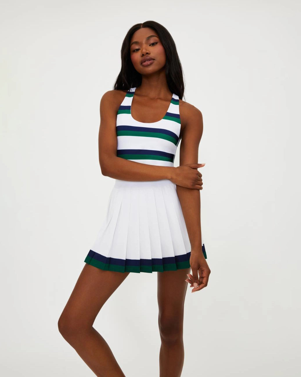 A woman wears a white pleated tennis skirt with navy and green stripe around the bottom