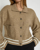 Woman wearing a beige knitted button down jacket with white trim