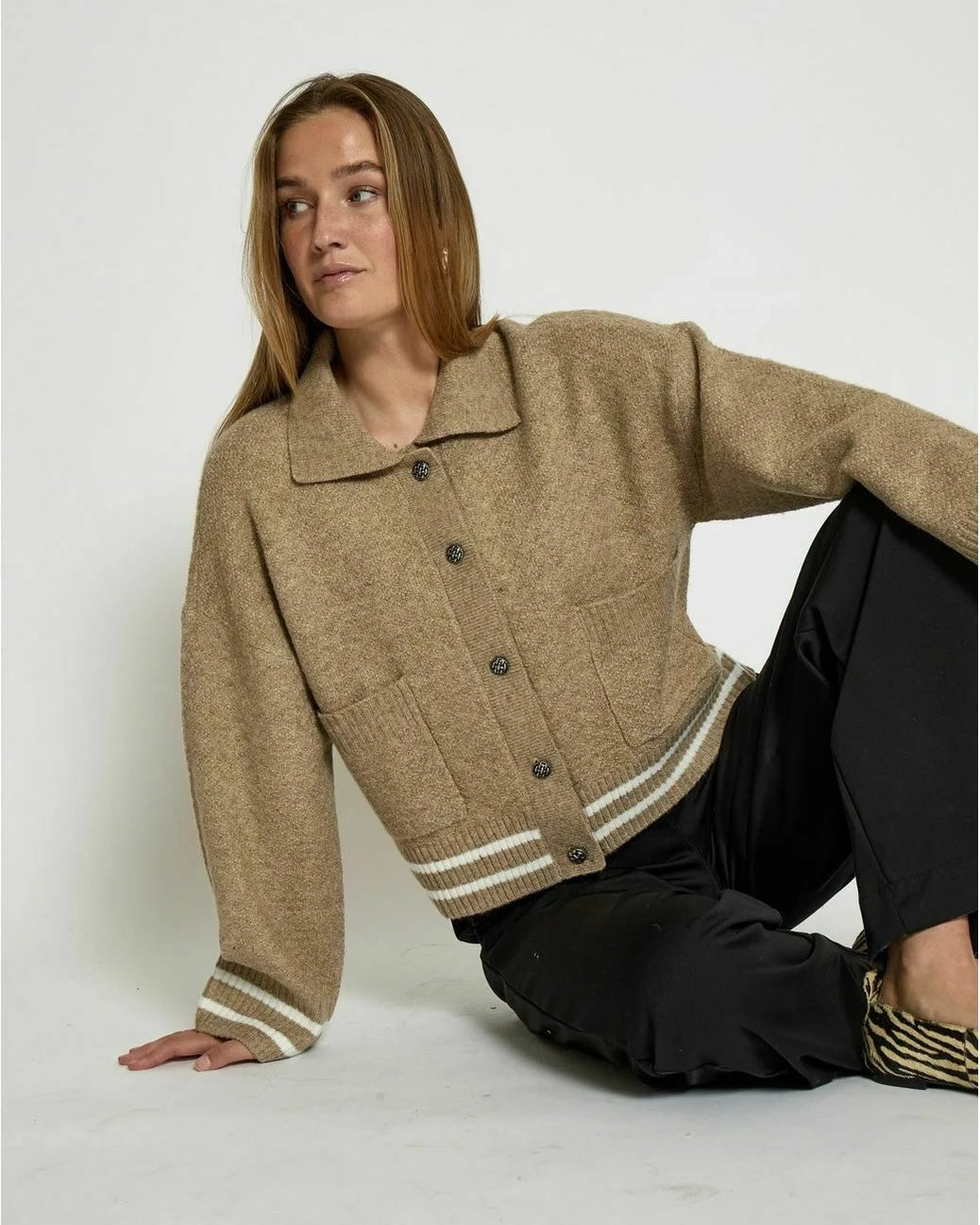 Woman wearing a beige knitted button down jacket with white trim
