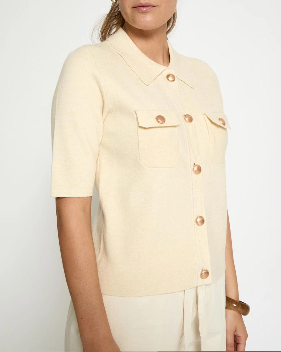 Woman wearing a cream short sleeve shirt with gold buttons