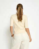 Woman wearing a cream short sleeve shirt with gold buttons