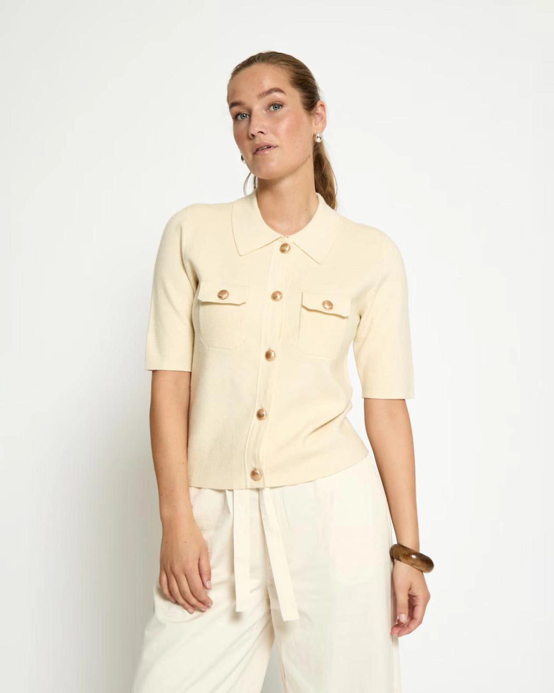 Woman wearing a cream short sleeve shirt with gold buttons