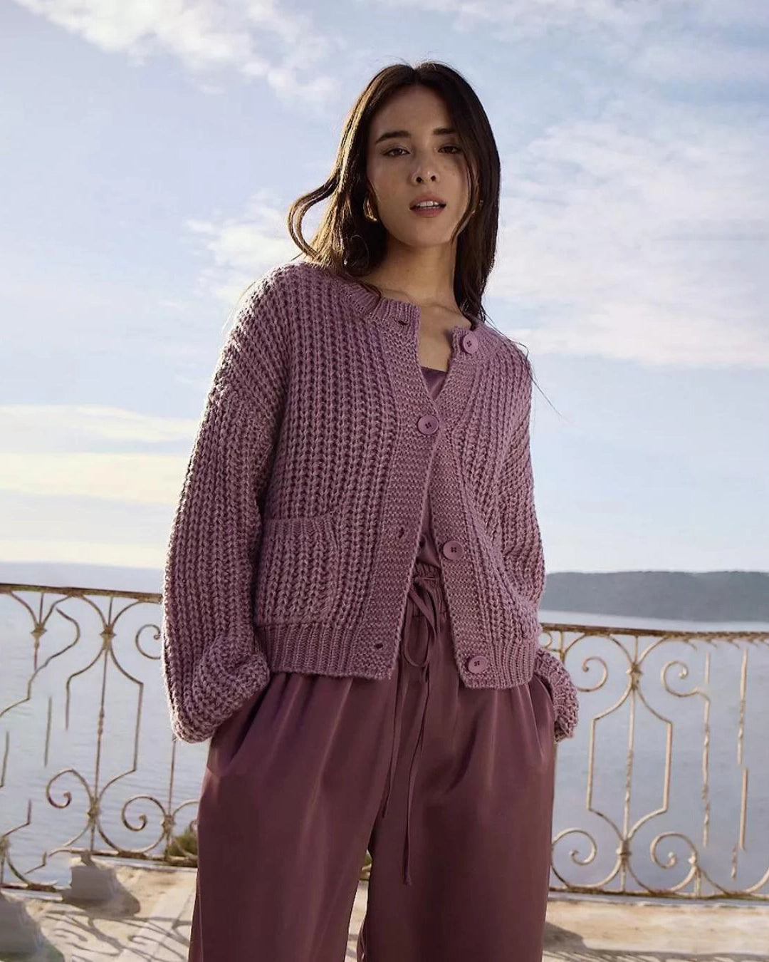 woman wearing a loose knit cardigan with large buttons and bubble sleeves in mauve purple