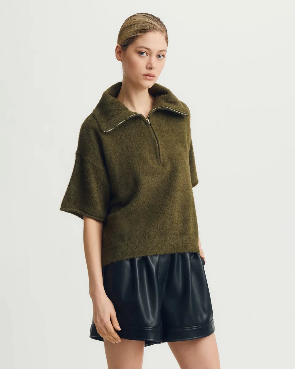 Woman wearing a green short-sleeve half zip sweater and black leather shorts