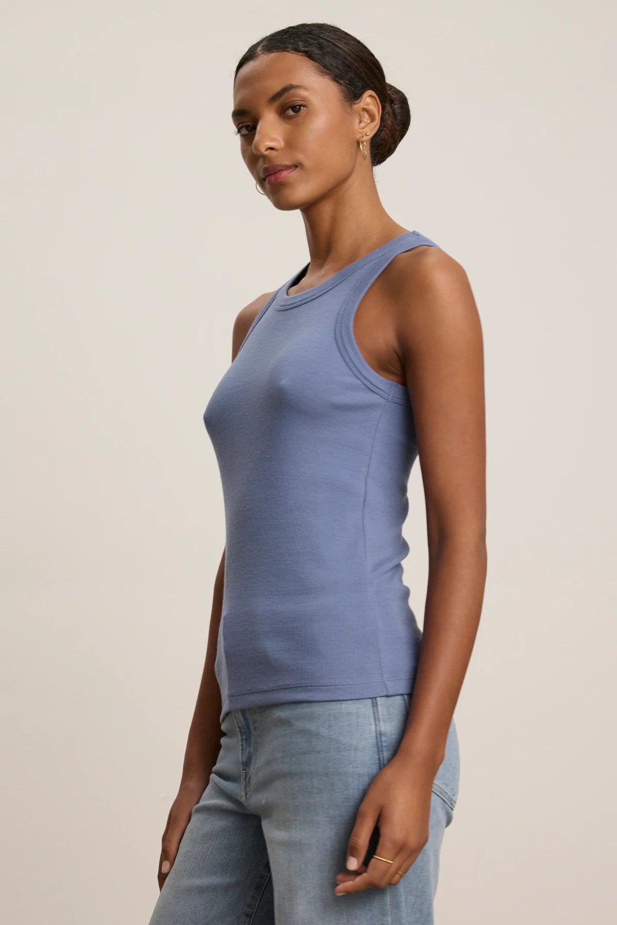 A woman wearing a blue ribbed tank top and grey trousers
