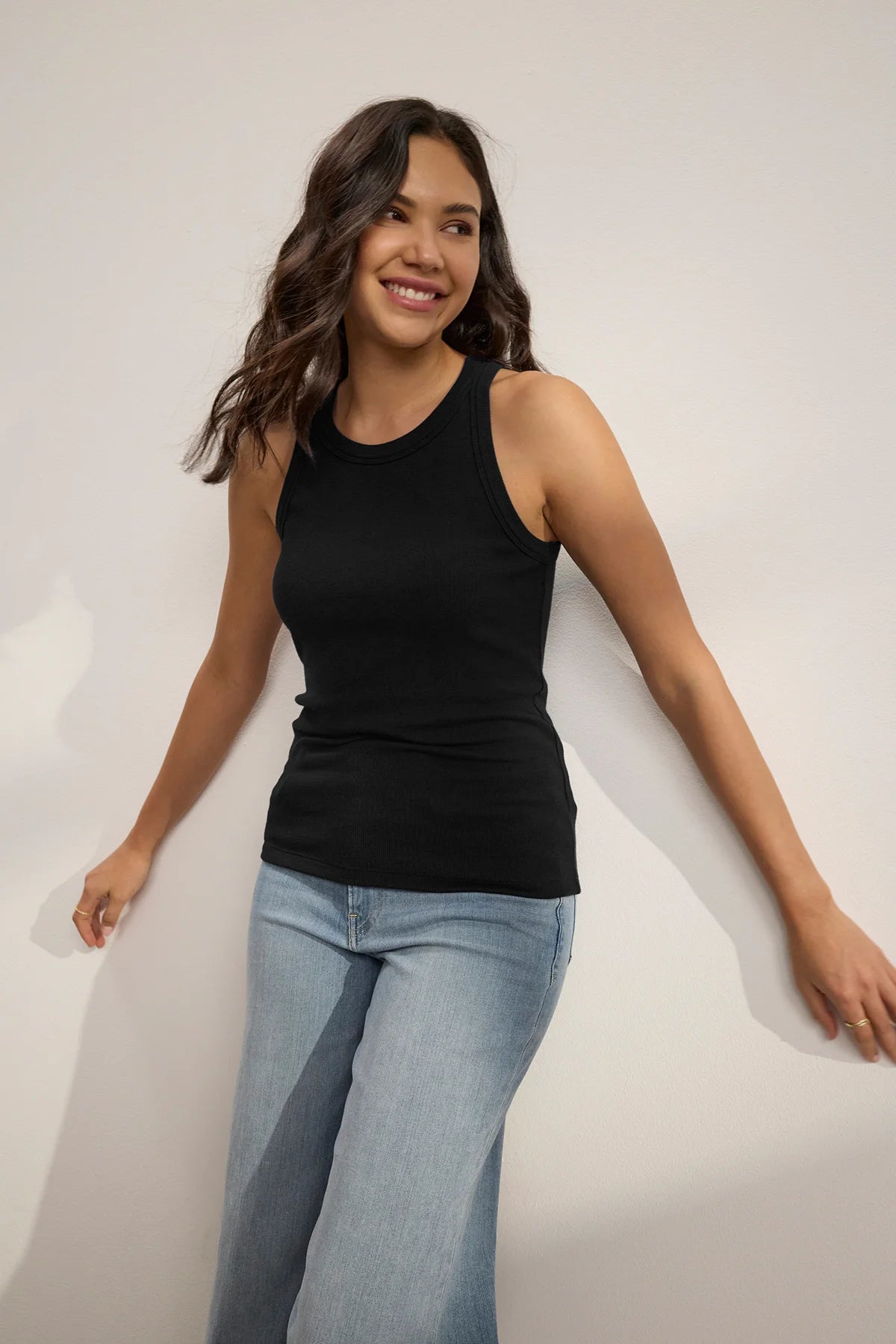 A woman wearing a black ribbed tank top and grey trousers