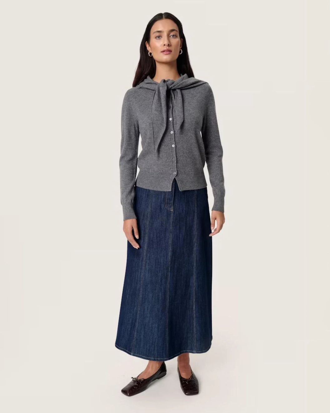 Woman wearing a grey button down cardigan sweater with a tie front scarf design