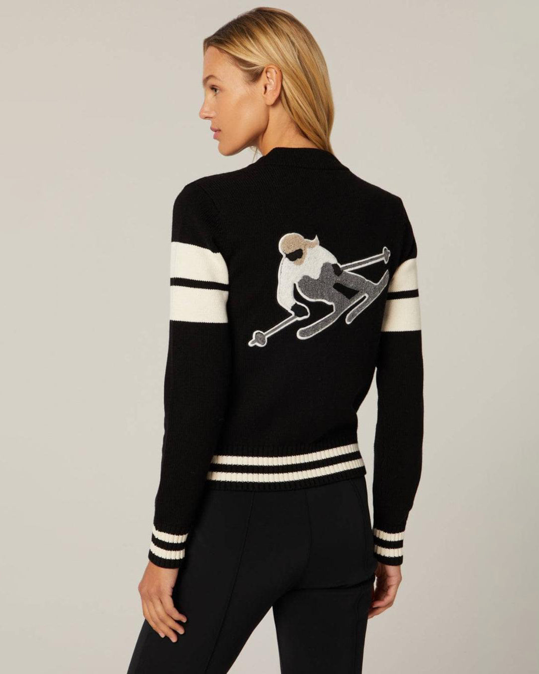 Woman wearing a black zip up cardigan jacket with white stripes and a skier on the back