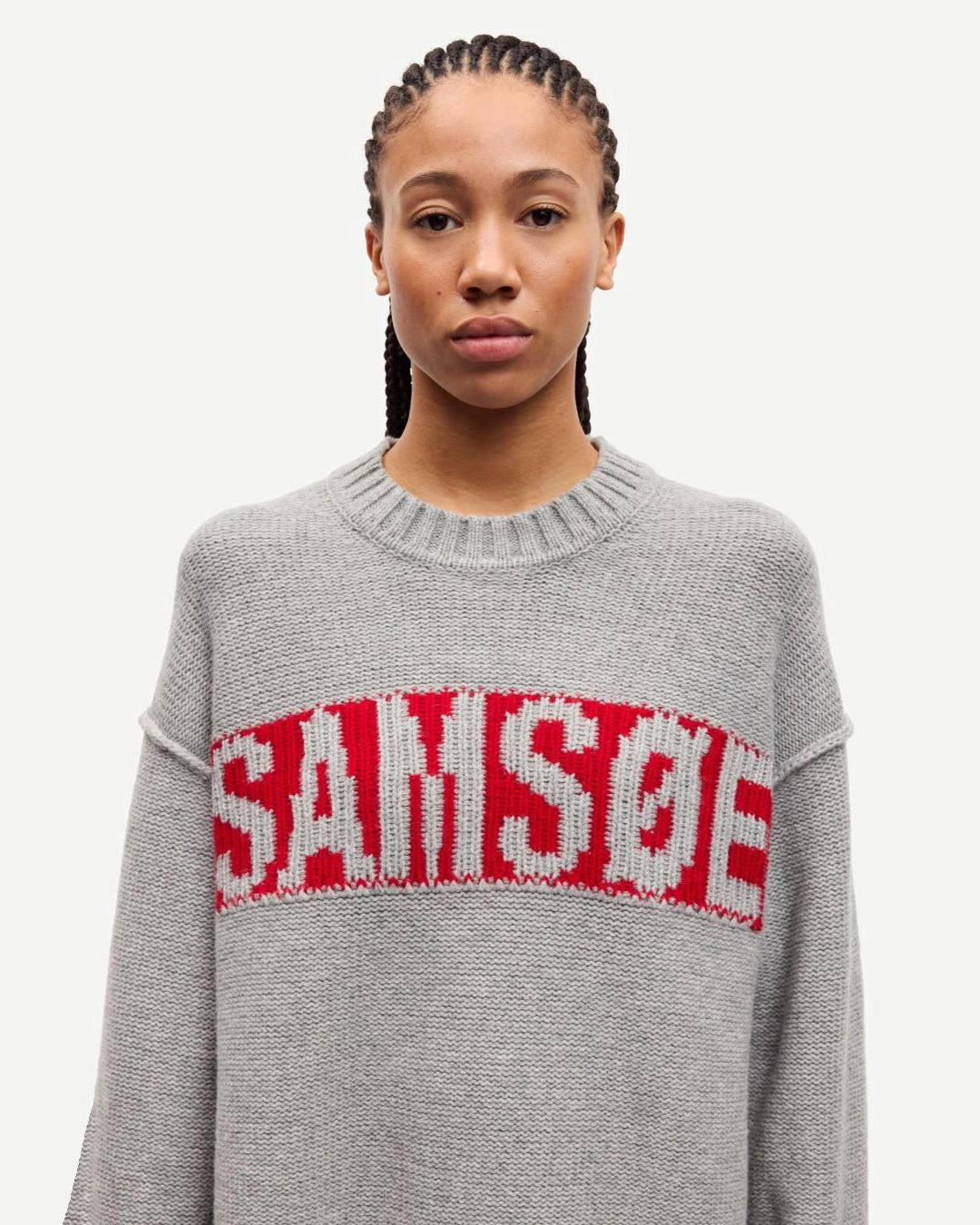 Person wearing a gray sweater with red text that says the brand 'SAMSOE'