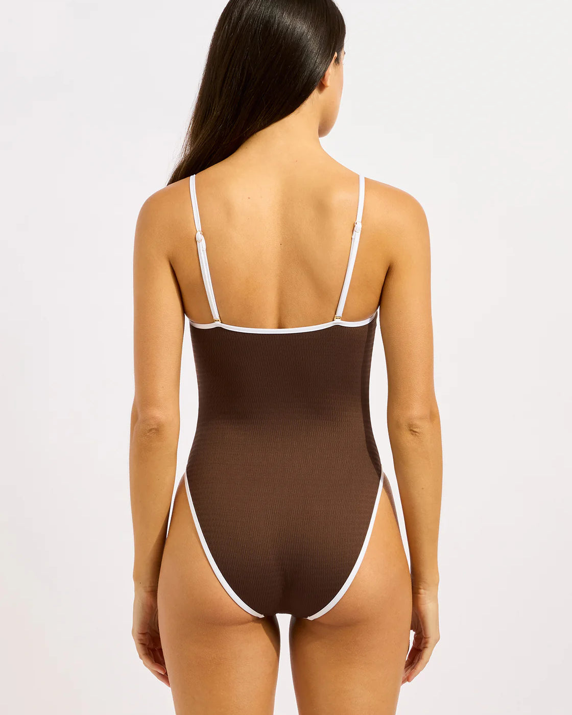 A woman wearing a brown ribbed one-piece swimsuit with thin white contrast trim and spaghetti straps by Seafolly