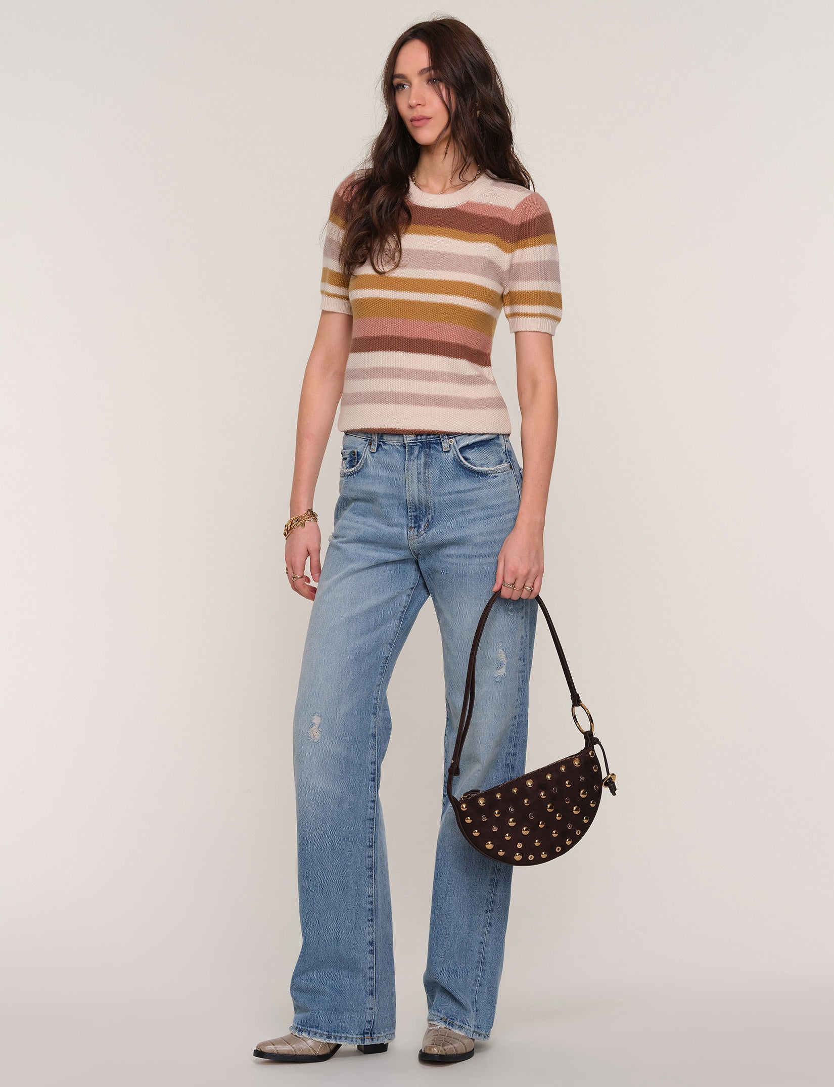 Woman wearing a striped shirt and jeans, holding a handbag against a plain background