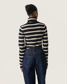 a woman wears a striped black and cream turtleneck polo pullover sweater