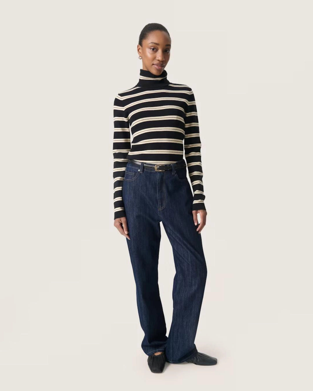 a woman wears a striped black and cream turtleneck polo pullover sweater