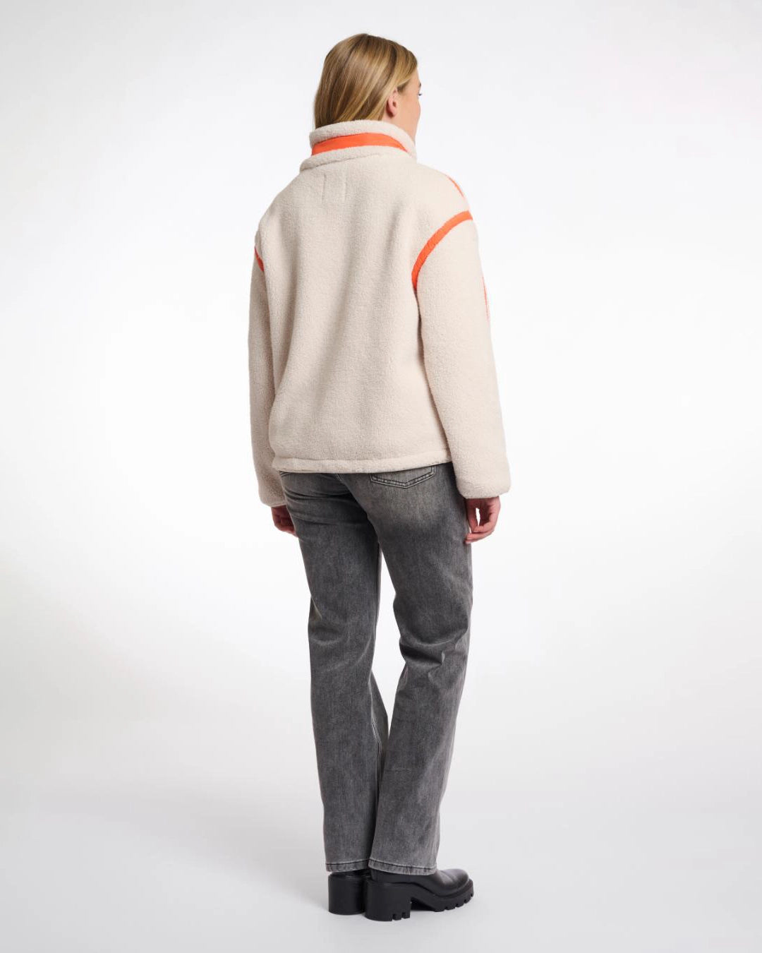 A woman wearing a teddy zip jacket in birch and orange pocket and lining