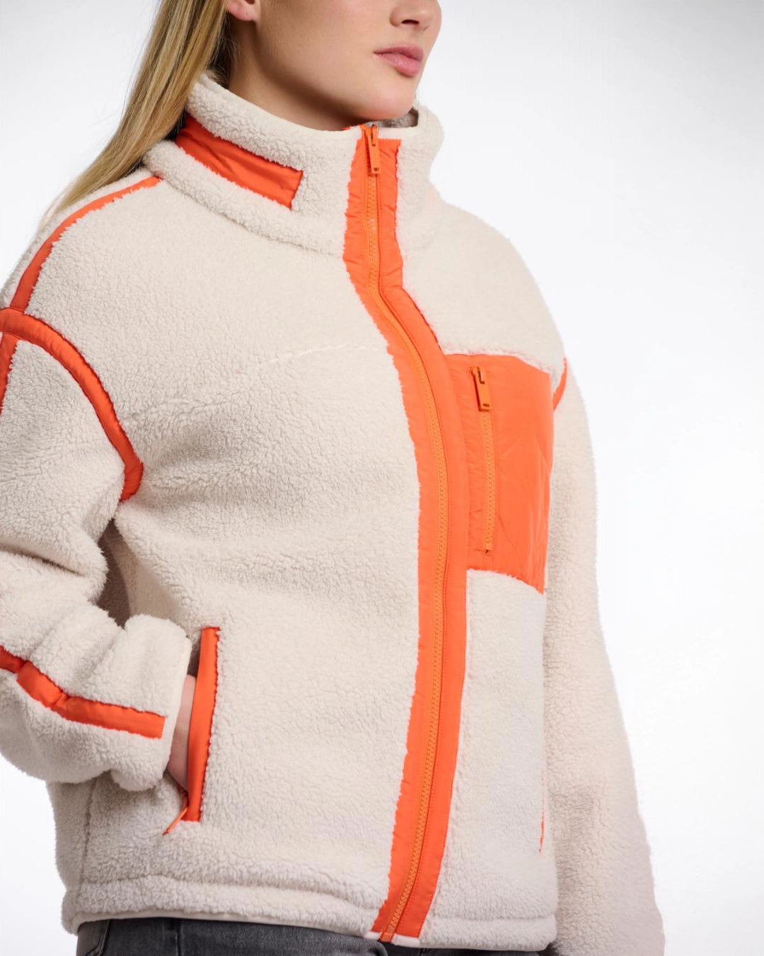 A woman wearing a teddy zip jacket in birch and orange pocket and lining